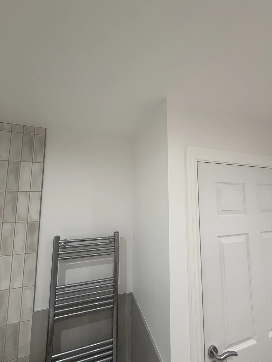 White painted bathroom walls and door beside grey tiles and chrome towel radiator