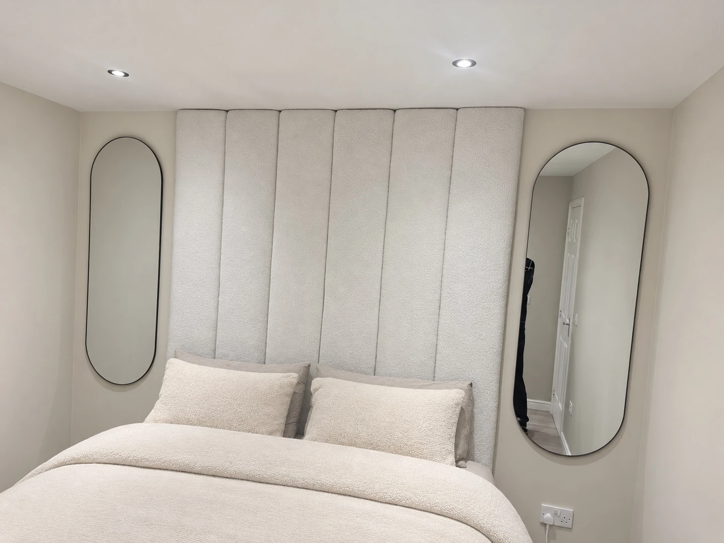 Cream upholstered headboard with tall vertical panels and oval mirrors